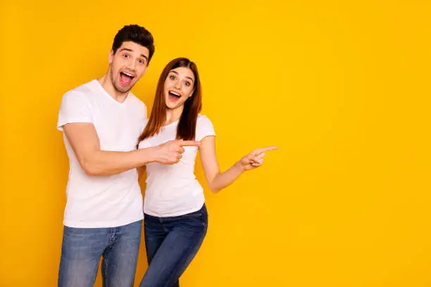 Photo of Close up photo beautiful she her he him his pair direct indicate fingers empty space great little low prices shopping shop mall store wear casual jeans denim white t-shirts isolated yellow background