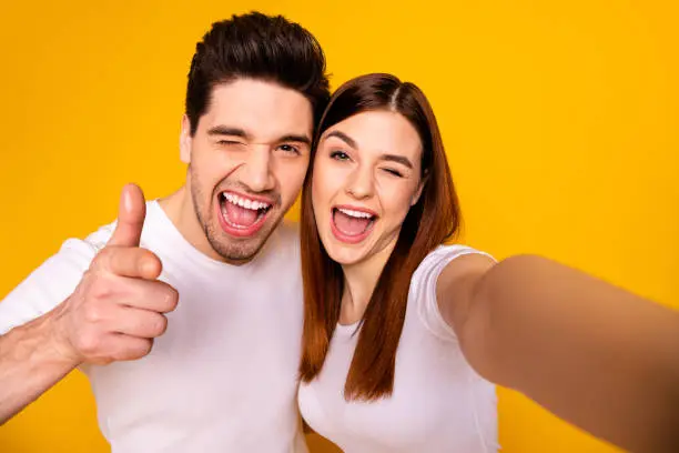 Self-portrait of his he her she two nice attractive lovely charming cute stylish trendy cheerful optimistic people showing thumbup isolated over vivid shine bright yellow background.