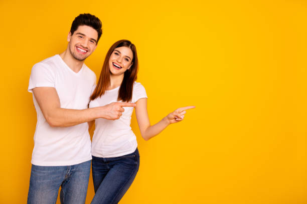 istock Close up photo beautiful she her he him his pair wondered direct indicate fingers empty space sale discount great little low price wear casual jeans denim white t-shirts isolated yellow background 1147554198
