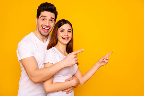 istock Close up side profile photo beautiful she her he him his pair wondered direct indicate fingers empty space sale discount great little low price wear casual white t-shirts isolated yellow background 1147554555
