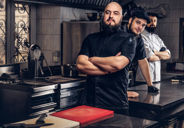 istock Team of professional bearded cooks dressed in uniforms standing in kitchen. 1147563511