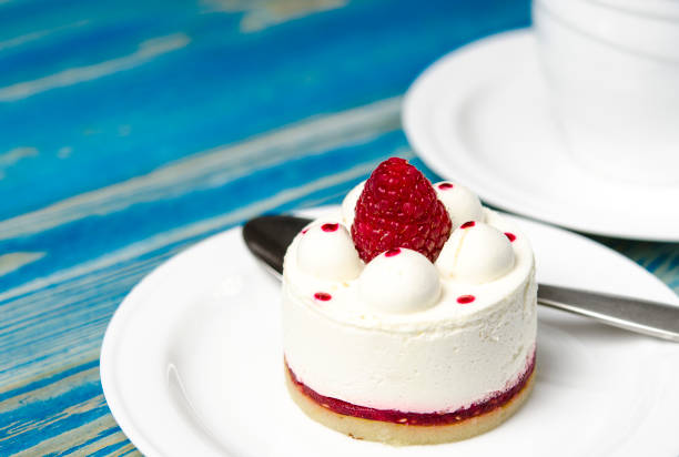 istock White airy cake with raspberry layer and raspberry berry lies on a white round plate next to a white cup, which stands on a blue table 1147566697