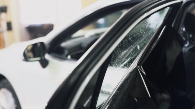 Close-up worker installs tint film for car glass, slow-motion.