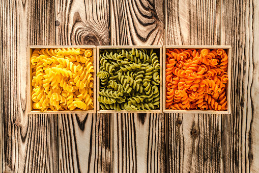 Multi-coloured pasta in the form of spirals lies in square wooden boxes that stand on a wooden table
