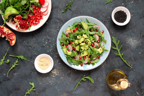 istock Ingredient for making salad on dark background. Vegetable salad in plate, avocado, arugula, pomegranate, radish and sesame. 1147575217