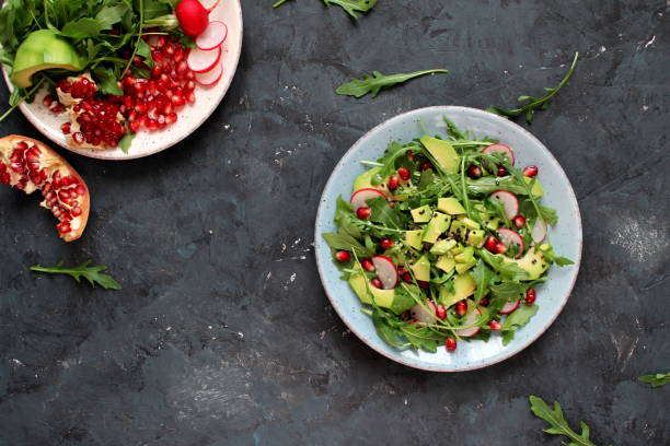 istock Ingredient for making salad on dark background. Vegetable salad in plate, avocado, arugula, pomegranate, radish and sesame. 1147575223