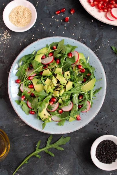 istock Ingredient for making salad on dark background. Vegetable salad in plate, avocado, arugula, pomegranate, radish and sesame. 1147575352