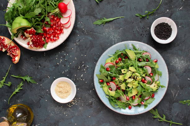 istock Ingredient for making salad on dark background. Vegetable salad in plate, avocado, arugula, pomegranate, radish and sesame. 1147575376