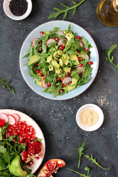 istock Ingredient for making salad on dark background. Vegetable salad in plate, avocado, arugula, pomegranate, radish and sesame. 1147575414
