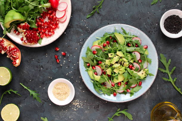 istock Ingredient for making salad on dark background. Vegetable salad in plate, avocado, arugula, pomegranate, radish and sesame. 1147575434