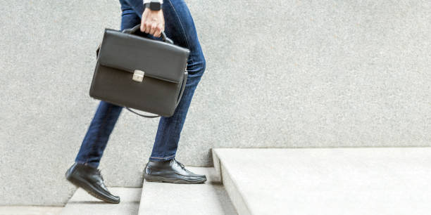 Businessman with black briefcase in hand walking up on stairs. Businessman with black briefcase in hand walking up on stairs. business goal, improvement, progress, Increase and growth concept. Outdoor closeup shot. in grey wall copy space. walking steps stock pictures, royalty-free photos & images