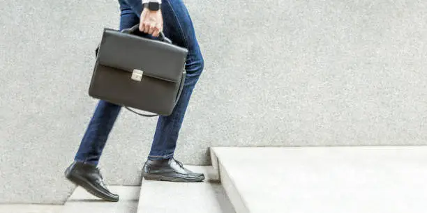 Photo of Businessman with black briefcase in hand walking up on stairs.