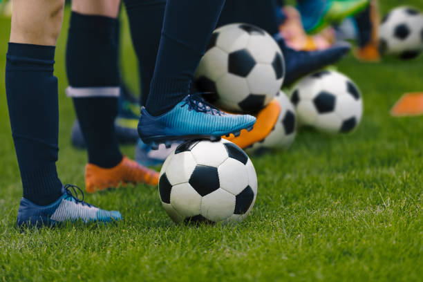 sesión de entrenamiento de fútbol junior. jugadores de pie en fila con clásicas bolas negras y blancas. práctica de jóvenes en campo de fútbol. imagen de close-up de ángulo bajo de soccer boys. antecedentes de educación futbolística - soccer child coach childhood fotografías e imágenes de stock