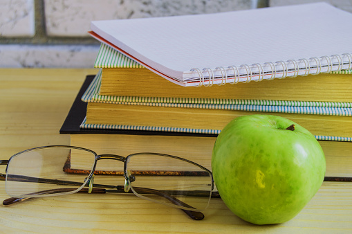 Teacher's Day concept and back to school, green Apple, book, laptop, reading glasses and pen on wooden table, sunlight.