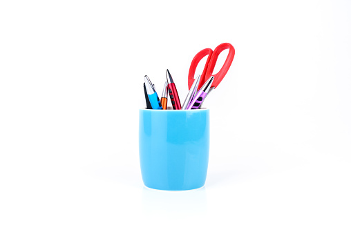 Colorful pens and orange scissors are in blue mug isolated on white background.