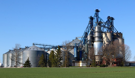 Several grain storage bins and grain dryer with blue sky and grass