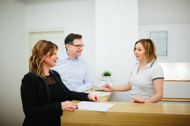 At clinic Positive young couple talking with secretary at reception in the clinic sports training clinic stock pictures, royalty-free photos & images