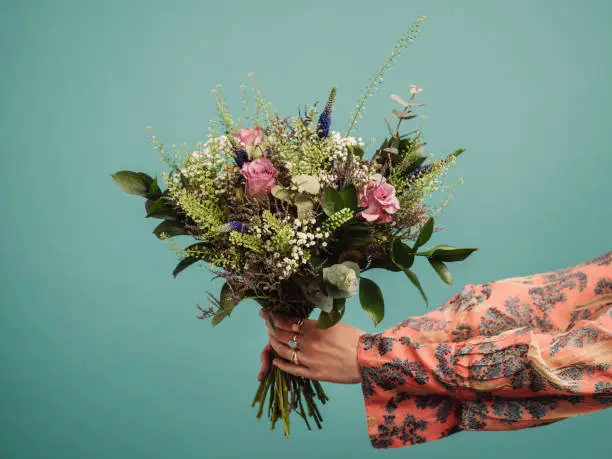 Woman holding a big bouquet of flowers, arms only
Photo of hands and flowers in studio against turquoise