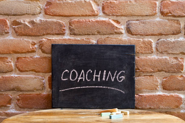 Chalk board with the word COACHING drown by hand on wooden table on brick wall background. stock photo