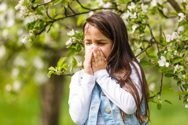 little girl is blowing her nose near spring tree in bloom - spring child green small imagens e fotografias de stock