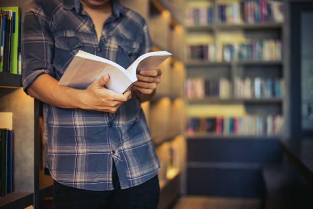 istock Man student reading a book in a library,Young man opening and reading a book, close up, warm retro tone. 1147595258