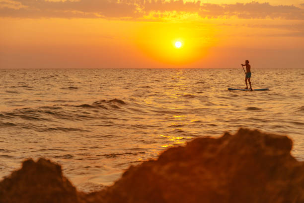 istock Man floating on paddle board in sea at sunset. 1147603682