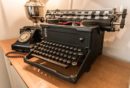 Old typewriter with old phone on the table with lamp  on the background