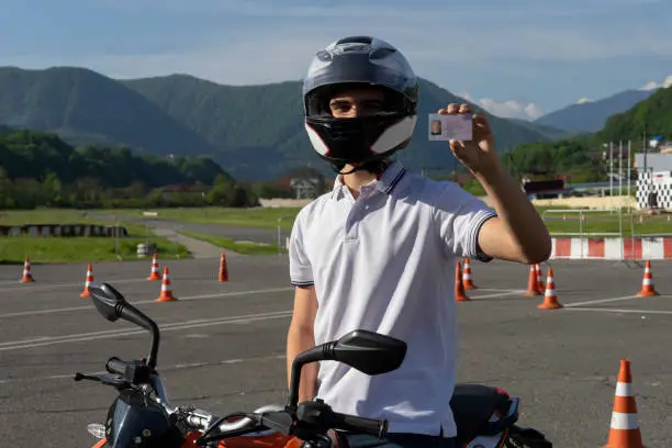 Photo of Young man in a helmet on the motorbike is showing driving license