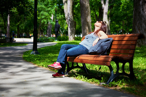 Redhead woman sunbathing in the park and sitting on the bench