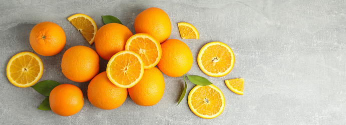 Many ripe oranges with leaves on grey table, top view