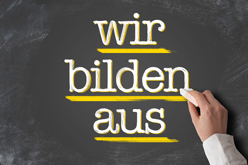 text WIR BILDEN AUS, German for we train apprentices, written on blackboard