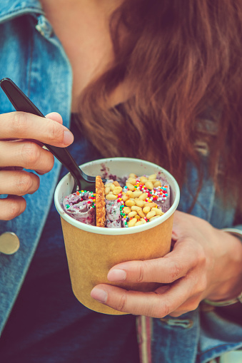 Young woman holding rolled ice-cream or yogurt with fruits or berries, cookies, candy and mint