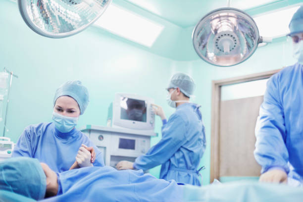 arzt hält hand des patienten im operationssaal - operationskittel stock-fotos und bilder