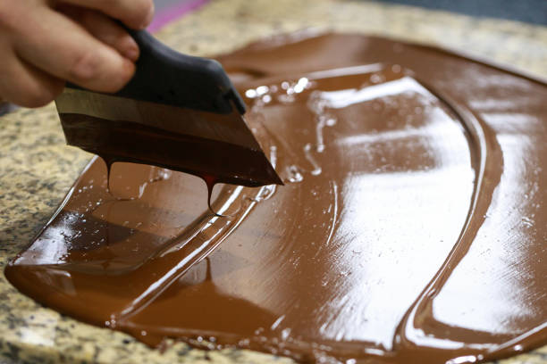 istock Chocolatier with a spatula is stirring the tempered liquid chocolate on a granite table 1147640431