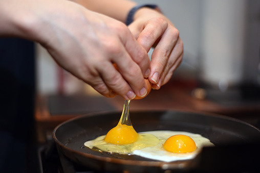 Hands cracking eggs into pan