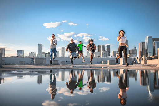Men and women jogging on rooftop in Los Angeles against sky. Full length of young friends are training in city. They are in sportswear.