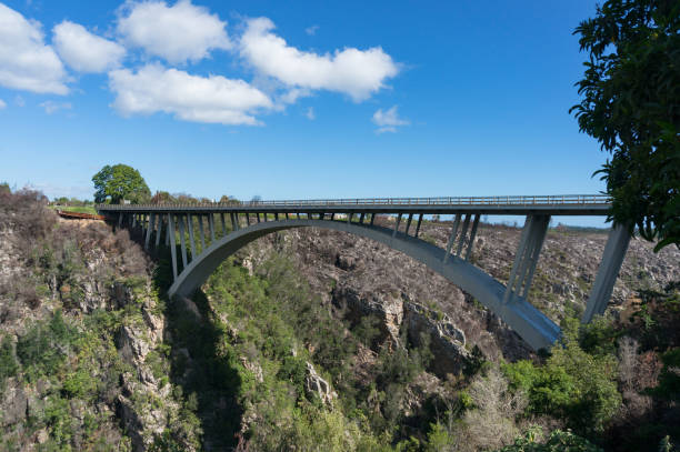 Drone shot view of a river mouth running from the mountains and a road bridge running across it on a sunny day.  Palmiet River Bridge, Western Cape, South Africa.