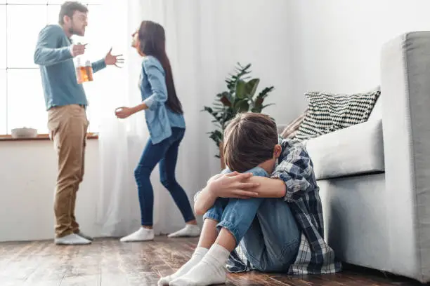 Family social problems domestic violence concept boy sitting crying near sofa while parent fighting shouting