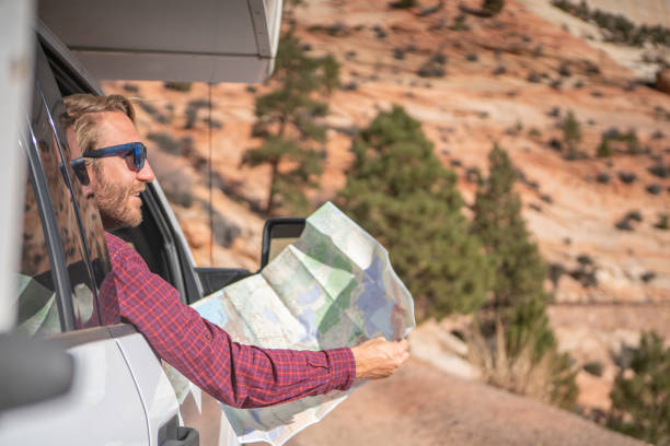 istock Road trip concept; Young man inside camper-van looking at road map for directions exploring national parks and nature ready for adventure. 1147670492