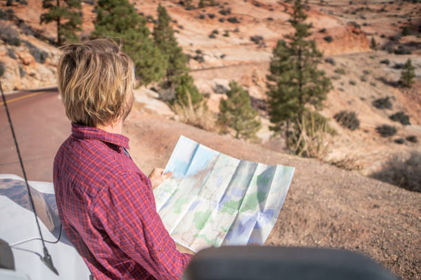 istock Road trip concept; Young man outside campervan looking at road map for directions exploring national parks and nature ready for adventure. 1147672163