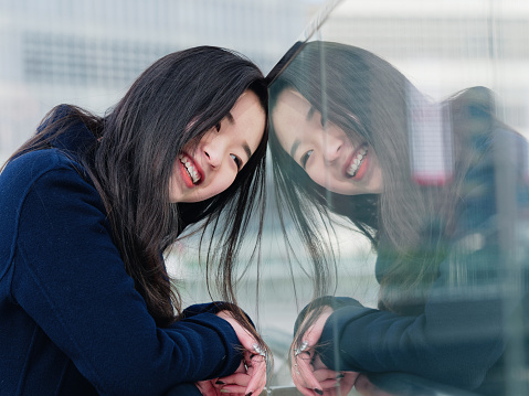 Portrait of a beautiful Chinese girl smiling with her mirror image in glass.