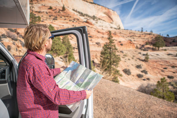 istock Road trip concept; Young man outside campervan looking at road map for directions exploring national parks and nature ready for adventure. 1147673089