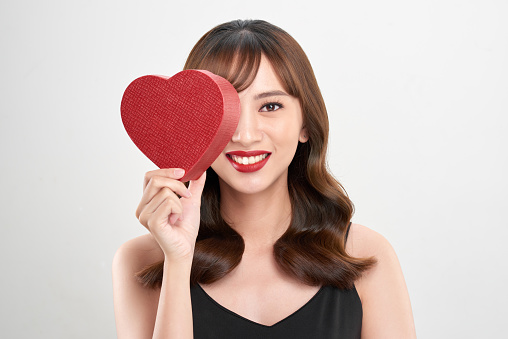 Cute young woman holding pink heart symbol against pale white background