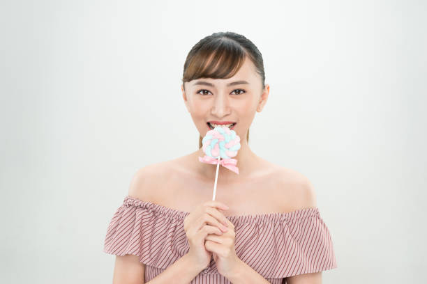 Blonde young girl with pigtails holding multi colored lollipop looking at camera dressed with pink sweater shot against pink background. The composition is at the left leaving useful copy space for text and/or logo at the right. Predominant color is pink. DSRL studio photo taken with Canon EOS 5D Mk II and Canon EF 70-200mm f/2.8L IS II USM Telephoto Zoom Lens