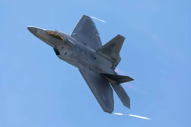 Close view of a F-22 Raptor in a  high G maneuver, with condensation trails forming  at the wings tip and afterburners on
