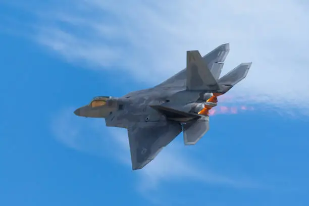 Very close tail  view of a F-22 Raptor against clouds, with afterburners on and the jet stream visible behind the aircraft