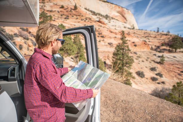 istock Road trip concept; Young man outside campervan looking at road map for directions exploring national parks and nature ready for adventure. 1147682783