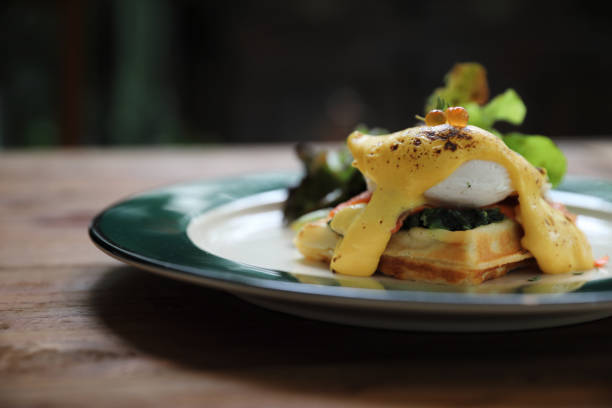 Breakfast food egg benedict , poached egg with yellow sauce with waffle and smoked salmon on wood background