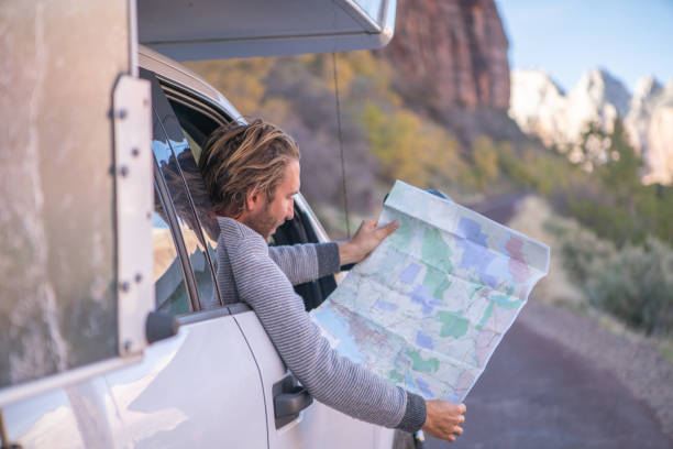istock Road trip concept; Young man inside campervam looking at road map for directions exploring national parks and nature ready for adventure. 1147693650