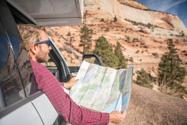 istock Road trip concept; Young man inside campervam looking at road map for directions exploring national parks and nature ready for adventure. 1147697274